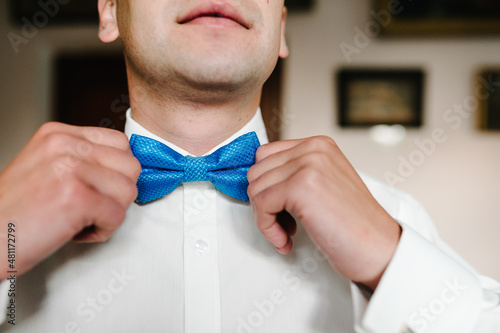 Fashion photo of a man, Man's hands touches bow-tie on a suit correcting his bowtie. Morning preparation groom at home.