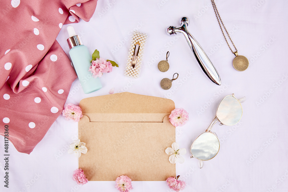 Feminine spring envelope mock up with pink flowers, sunglasses with sky reflection, accessories, massager, cosmetic gift on fabric white background. 8 of March concept