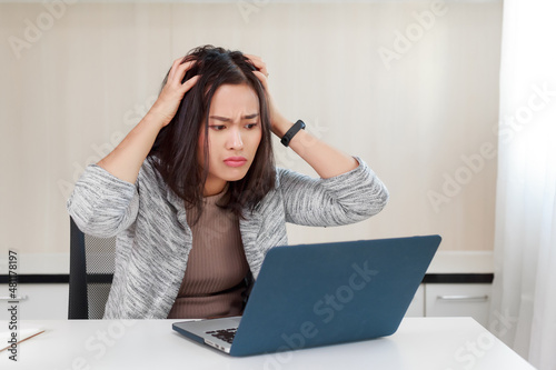 Upset Young Asian business woman having trouble work on laptop computer. Frustrate Secretary messed her hair with shocked and stressed emotion from the bad news sitting at desk in workplace.