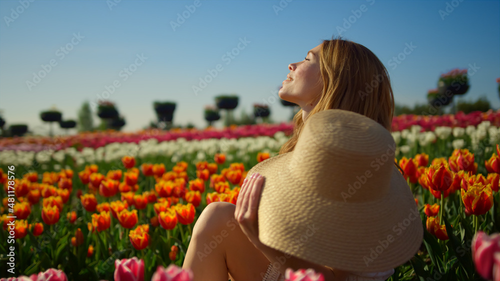 Fancy woman enjoying sun in tulip field. Relaxed girl turning face to sun.