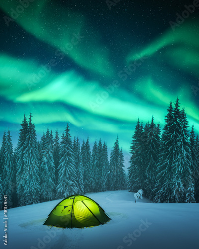 Yellow tent lighted from the inside against the backdrop of incredible starry sky with Aurora borealis. Amazing night landscape. Northern lights in winter field