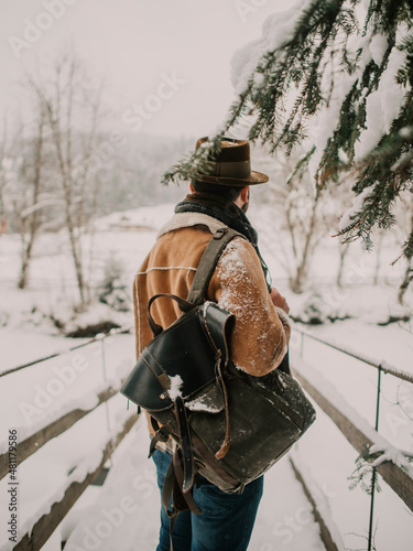 bearded man in a hat with backpack walking on a wooden bridge, snowy winter
