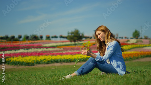 Beautiful girl sitting on grass in summer day. Relaxed girl enjoying wild flower