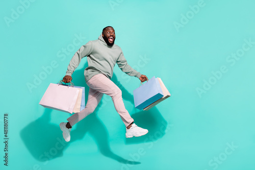 Full length body size view of attractive cheery trendy guy jumping running carrying bags isolated over vivid teal turquoise color background