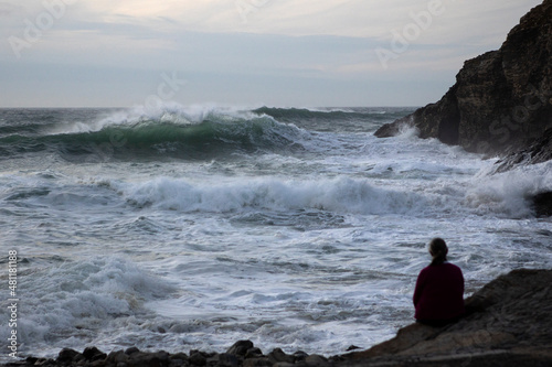A woman watches waves coming in from Atlantic swells at Chapel Porth, Cornwall