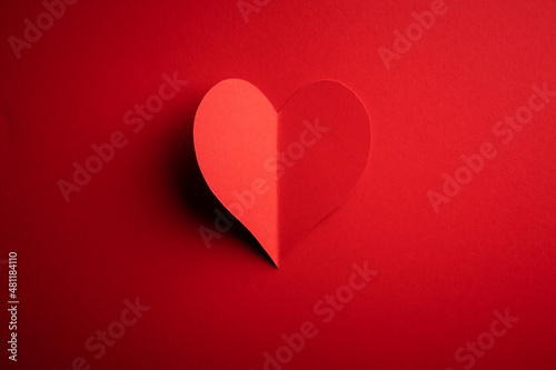 Creative Valentines Day postcard design with red paper heart on red cardboard background. Valentine day and love concept
