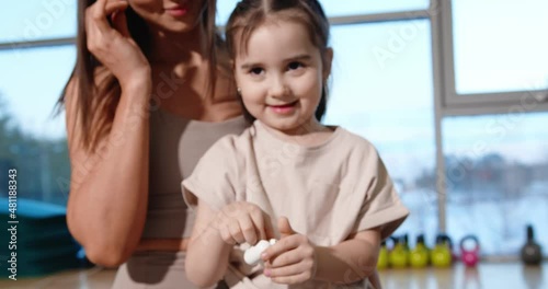 Cheerful mom with daughter listening to music through wireless headphones in the gym. Slow motion. Prores High Quality.