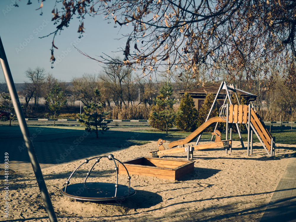 Fototapeta premium The morning, autumn sun illuminates the playground, there is a small carousel, swings and slides, there is no one, autumn mood
