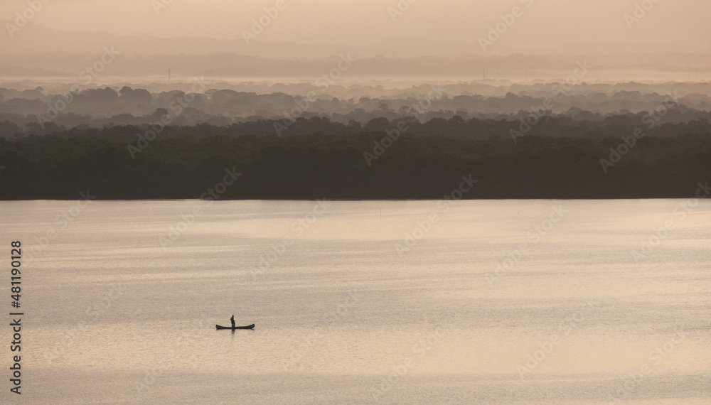 Fisherman on a small boat working in exotic land with immense backdrop of trees in mountains Fisherman on a small boat working in exotic land with immense backdrop of trees in mountains
