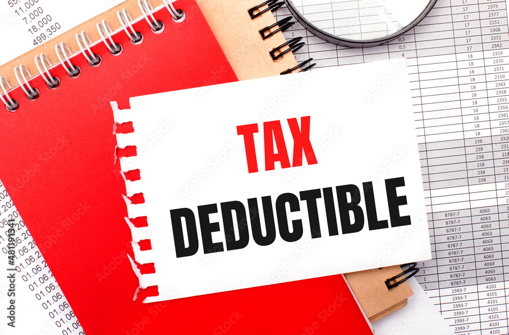 On a light background - reports, a magnifying glass, brown and red notepads, and a white notepad with the text TAX DEDUCTIBLE. Business concept