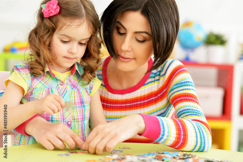 Fototapeta premium Portrait of mother with little daughter collecting puzzle