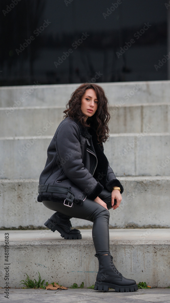 Girl on the steps. Stylish appearance. Total black. Girl with curly hair. Black jacket, black sweater, eco leather leggings. Girl on the steps. Stylish appearance. Total black. Girl with curly hair. Black jacket, black sweater, eco leather leggings.