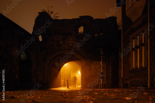 Illuminated cobbled street in an old town with light reflections on cobblestones, archway with ghostly figure photo