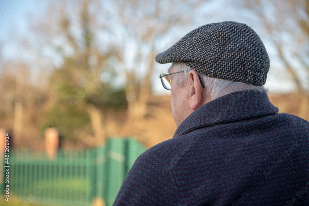 Rear view of senior mans head wearing a flat cap, taken outdoors in parkland with copy space Rear view of senior mans head wearing a flat cap, taken outdoors in parkland with copy space