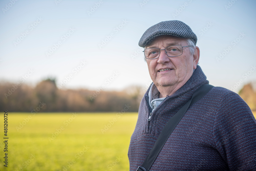 Happy senior man in green parkland, looking at camera, outdoors in the winter sun Happy senior man in green parkland, looking at camera, outdoors in the winter sun