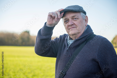 Happy senior man holding peak of cap, looking at camera, outdoors in the winter sun © stephm2506