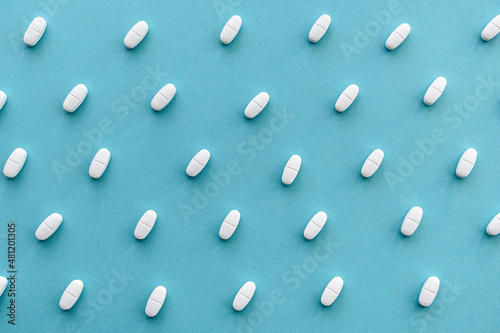 Blue medicine background with white scattered pills and tablet, macro. The concept of medicine, pharmacology and health.