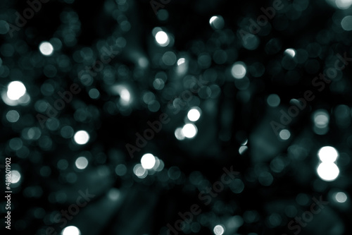 Blurred abstract green glitter texture. Tidewater Green colors. A little defocused bokeh christmas white and green lights on black background. Green bokeh glitter wallpaper for Christmas  New year.