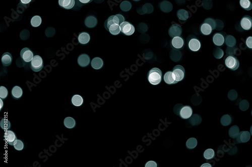 Defocused bokeh small green lights on black background. Blurred abstract green glitter texture. Green bokeh glitter wallpaper for Christmas, New year or festival background. Tidewater Green colors.