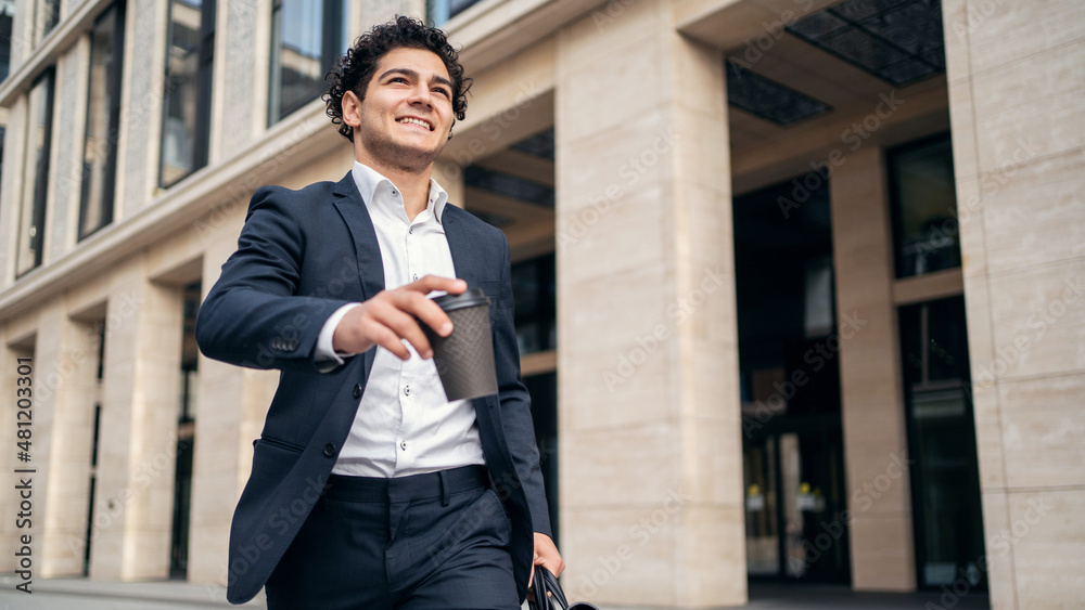 There is a confident satisfied man manager in an official suit holding a briefcase with documents and coffee in his hands There is a confident satisfied man manager in an official suit holding a briefcase with documents and coffee in his hands