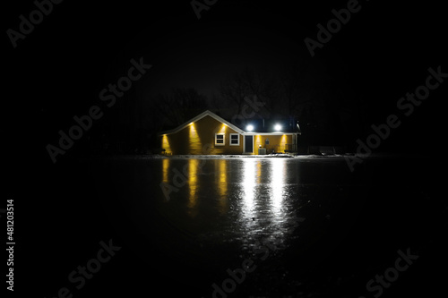 Fototapeta Naklejka Na Ścianę i Meble -  Yellow building in winter with lights reflecting on outdoor skating rink at night