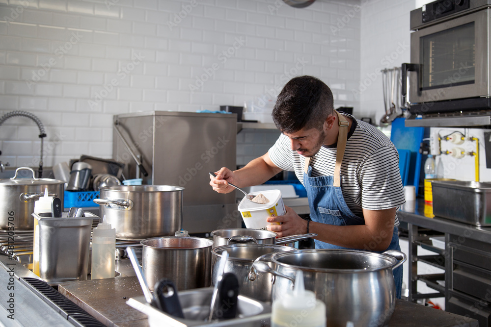 Ethnic male cook adding instant broth into saucepan during work in kitchen Ethnic male cook adding instant broth into saucepan during work in kitchen