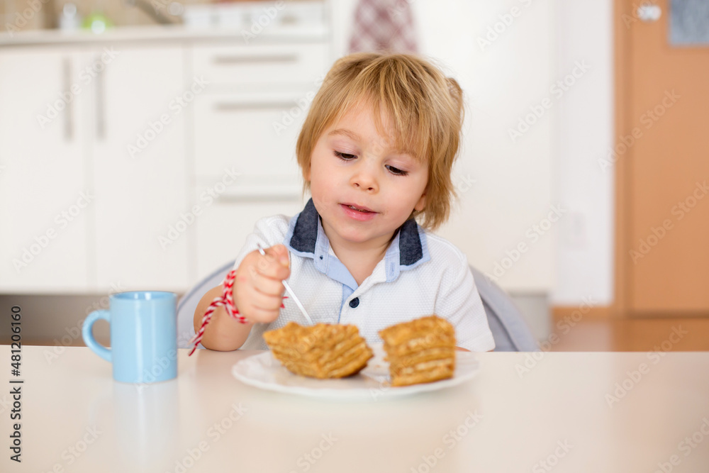 Cute preschool boy, blond child, eating piece of cake and drinking milk at home Cute preschool boy, blond child, eating piece of cake and drinking milk at home