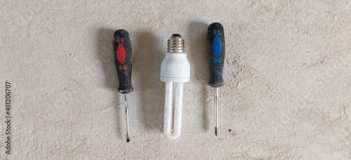 Two screwdrivers with colorful handles and an energy-saving lamp. Electricity, repair, house.