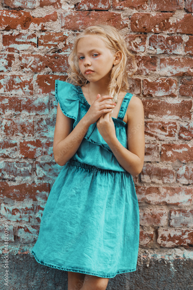 a young blonde girl in a blue dress poses against a brick wall a young blonde girl in a blue dress poses against a brick wall