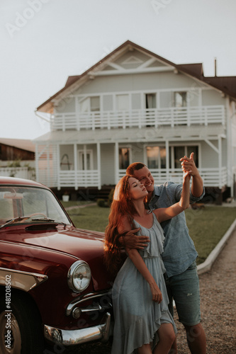 A young boy and a girl in love stand with their backs to a retro car holding hands.