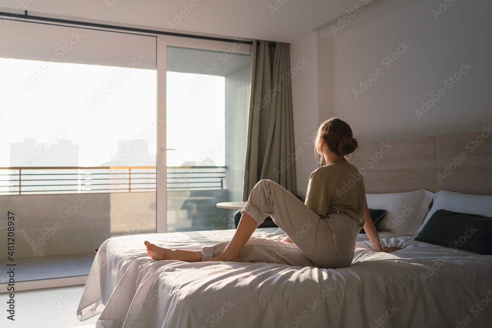 Young barefooted woman resting on bed in light apartment