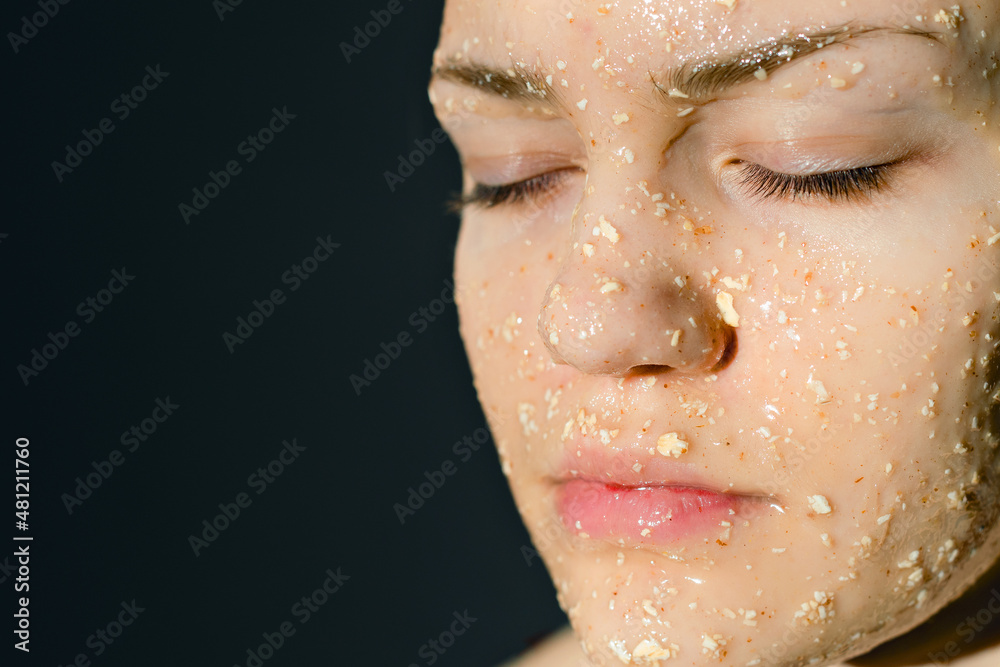 Face of girl with cosmetic mask of oatmeal with honey. Prevention of acne in adolescents. Woman's face with her eyes closed on dark background.