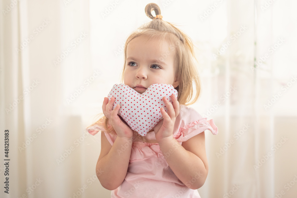 Little girl holding heart. Small heart shape pillow holding by little Caucasian girl smiling with innocence, at home. Concept of child, love and happiness, kindness, gift, handmade Valentine, familly Little girl holding heart. Small heart shape pillow holding by little Caucasian girl smiling with innocence, at home. Concept of child, love and happiness, kindness, gift, handmade Valentine, familly