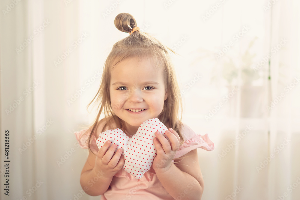 Little girl holding heart. Small heart shape pillow holding by little Caucasian girl smiling with innocence, at home. Concept of child, love and happiness, kindness, gift, handmade Valentine, familly Little girl holding heart. Small heart shape pillow holding by little Caucasian girl smiling with innocence, at home. Concept of child, love and happiness, kindness, gift, handmade Valentine, familly