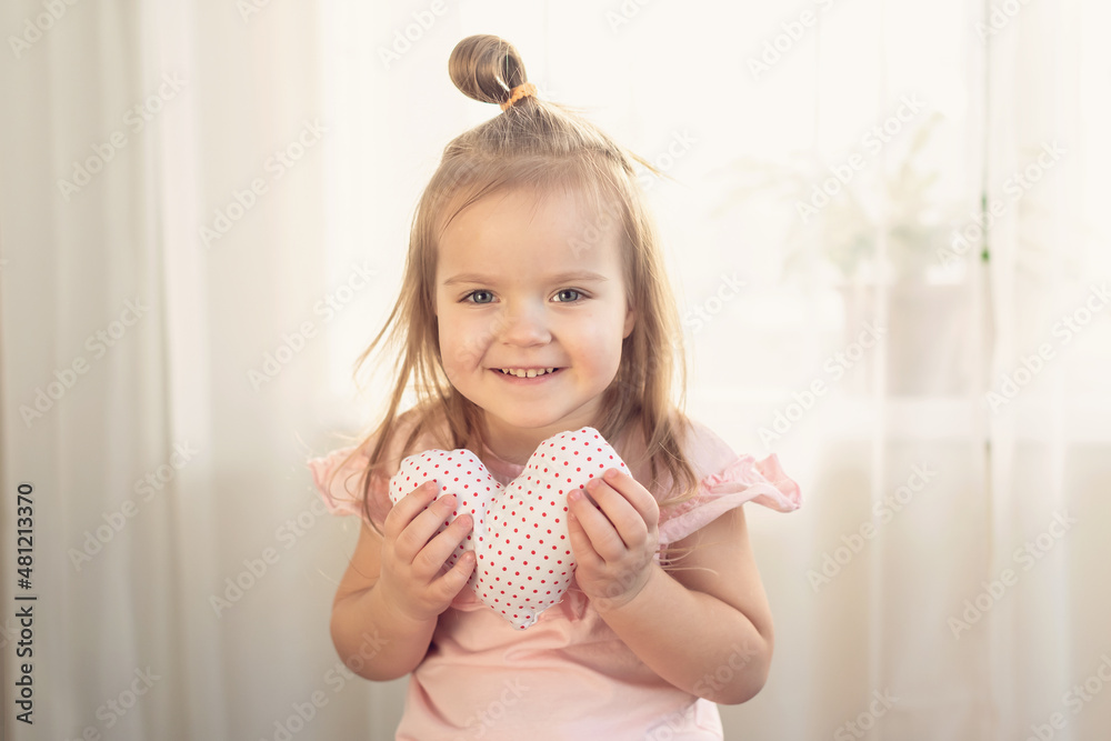 Little girl holding heart. Small heart shape pillow holding by little Caucasian girl smiling with innocence, at home. Concept of child, love and happiness, kindness, gift, handmade Valentine, familly Little girl holding heart. Small heart shape pillow holding by little Caucasian girl smiling with innocence, at home. Concept of child, love and happiness, kindness, gift, handmade Valentine, familly