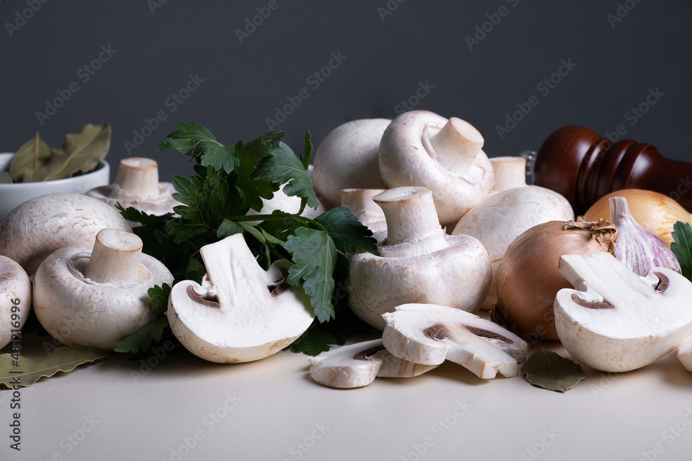Fototapeta premium Bunch of raw champignons with other cooking ingredients on table. Mushrooms are like vegetable protein. The concept of vegetarian and vegan food. Cooking at home or in restaurant.