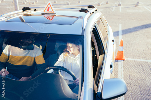 Carefully young woman in drivers seat of car taking driving lesson from instructor. Driving school concept. Driving instructor and woman student in examination car