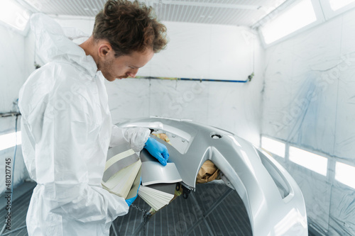 Male colourist selecting color of car bumper with paint matching samples