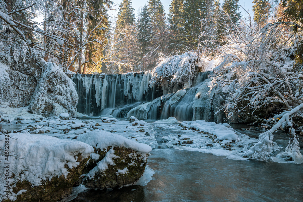 Obraz premium Gefrorener Wasserfall in einer schattigen Schlucht an einem sonnigen Wintertag.