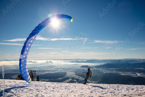 Paragliding in mountains, winter time with snow and blue sunny sky.