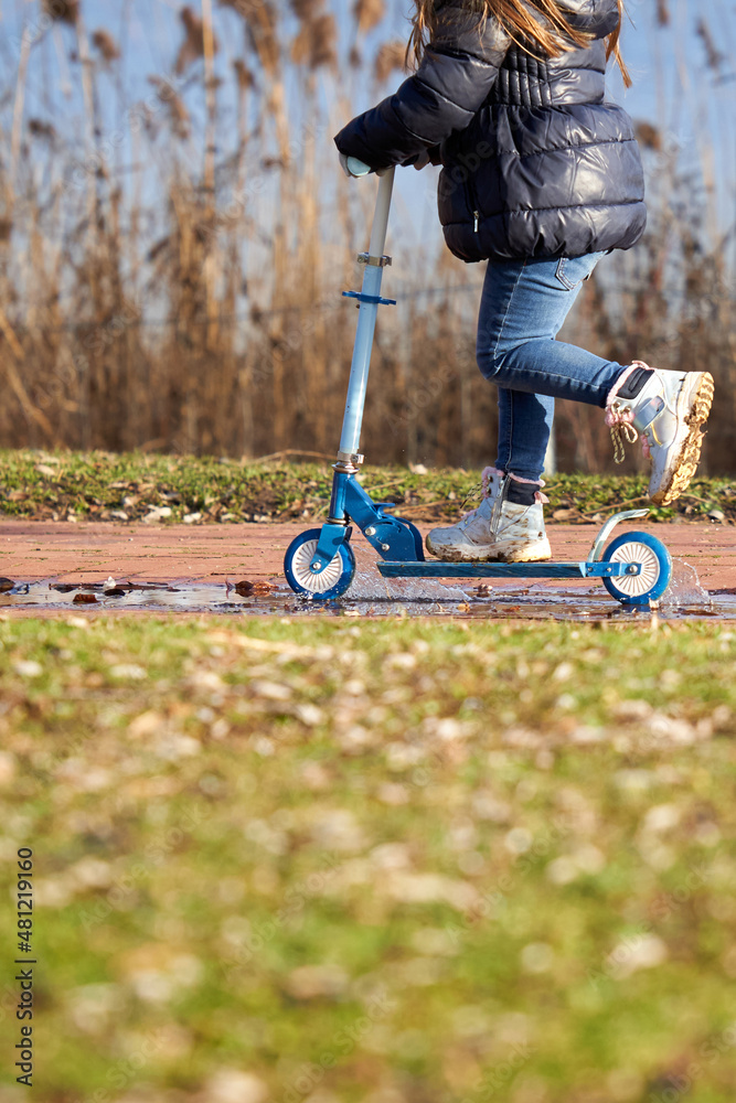 Obraz premium Girl riding scooter near lake. Child with blue sports equipment.