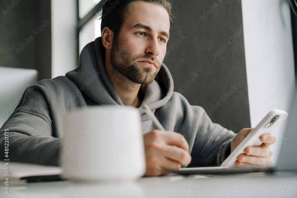 Young beard man using mobile phone while working with laptop Young beard man using mobile phone while working with laptop
