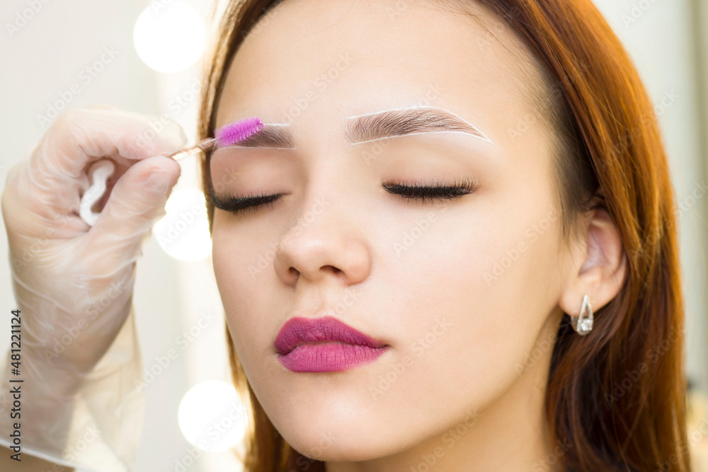 The makeup artist combs his eyebrows with a brush. Marking with a white pencil. Permanent makeup. Staining with henna paint.