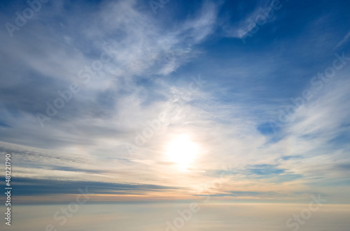 Aerial view of bright yellow sunset over white dense clouds with blue sky overhead.