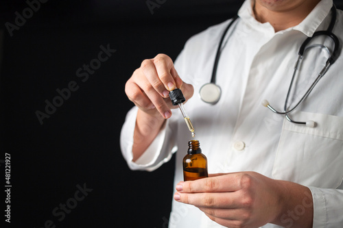 Male Caucasian doctor hands opening a glass pipette bottle and dropping droplets of CBD hemp oil, close-up shot.