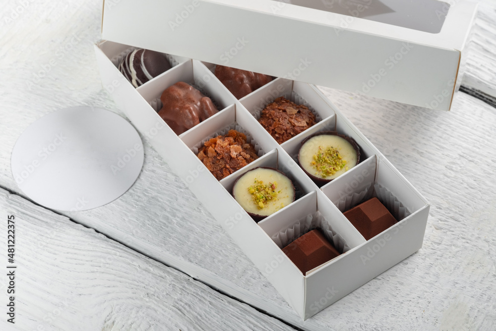 Handmade chocolates in a white gift box on a white wooden background. A variety of high quality candies Handmade chocolates in a white gift box on a white wooden background. A variety of high quality candies