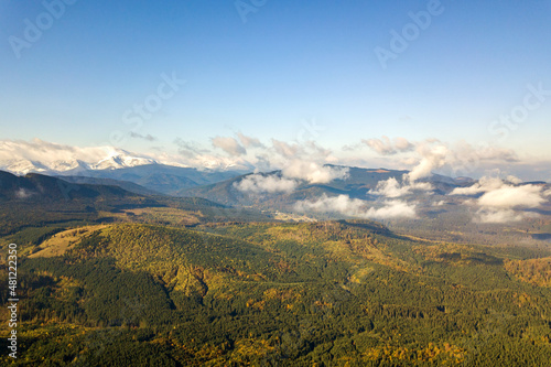 Aerial view of majestic mountains covered with green spruce forest and high snowy peaks.