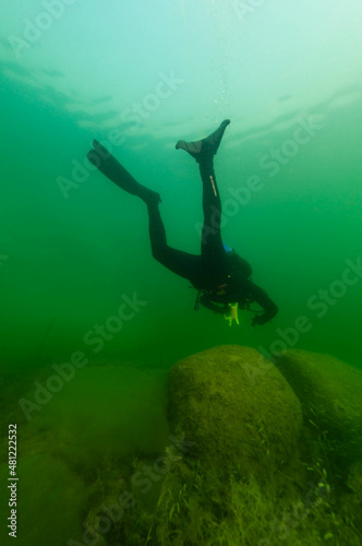 SCUBA diver exploring a cloudy inland lake with large boulders