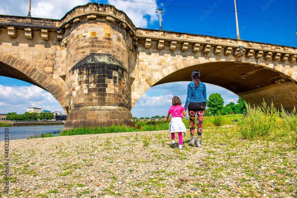 Back view of woman walking along the city river with her daughter on a sunny day.