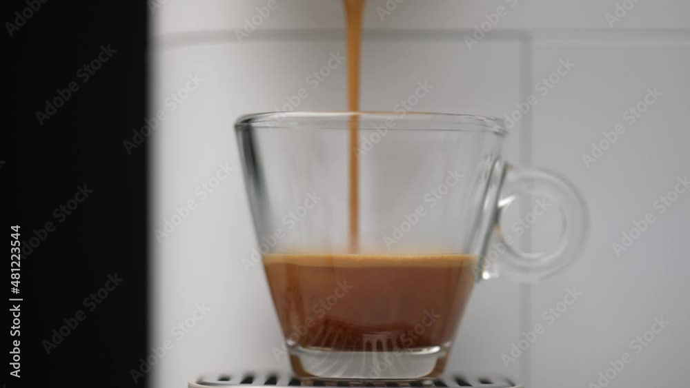 Dolly shot of a modern white automated coffee machine making espresso in a transparent glass coffee cup in a black background.